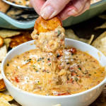 a hand dipping a cracker in a bowl of chili con queso.