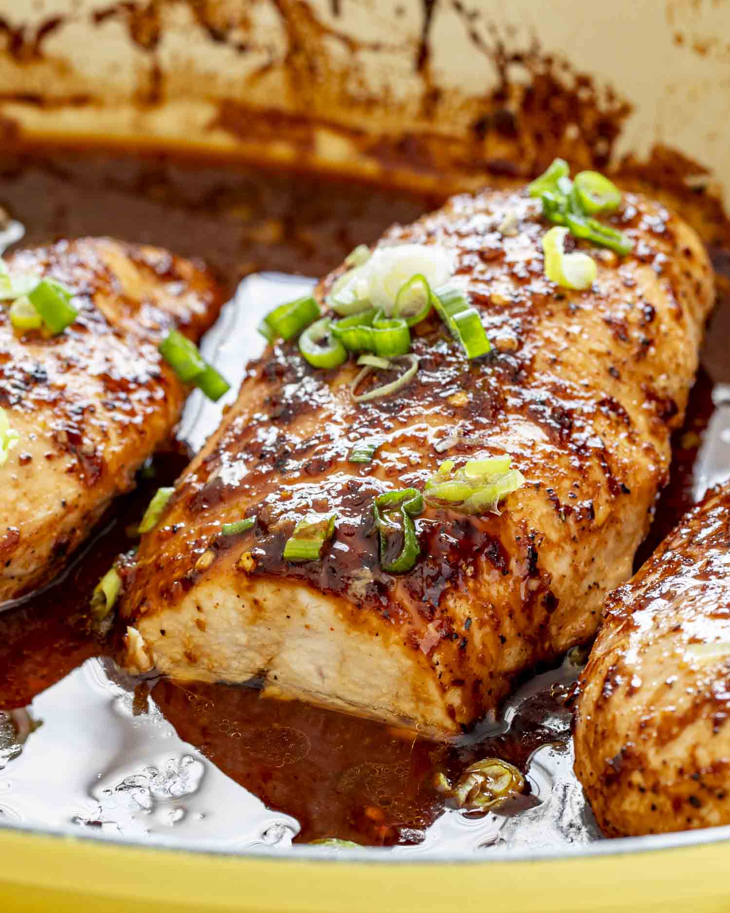 Juicy firecracker chicken breast sliced slightly open in pan, revealing tender inside and sticky chili-garlic glaze with green onions.
