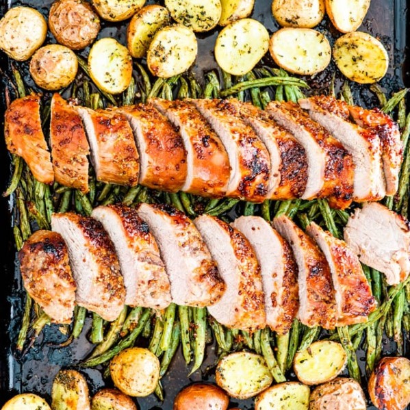 overhead shot of sliced honey mustard pork tenderloin on top of roasted green beans with roasted potatoes on either side
