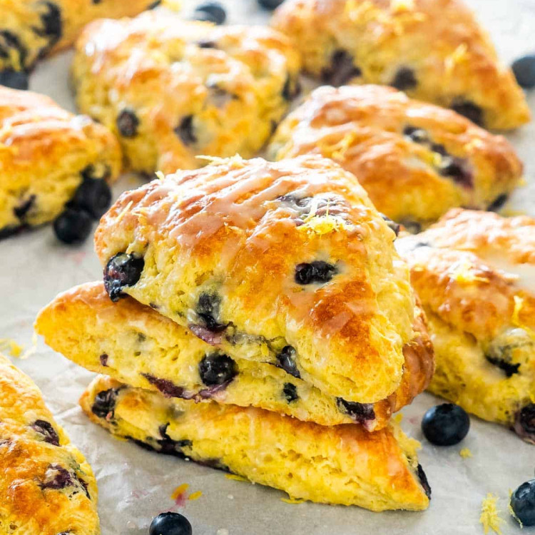 lemon blueberries scones scattered on a table with some blueberries in between.