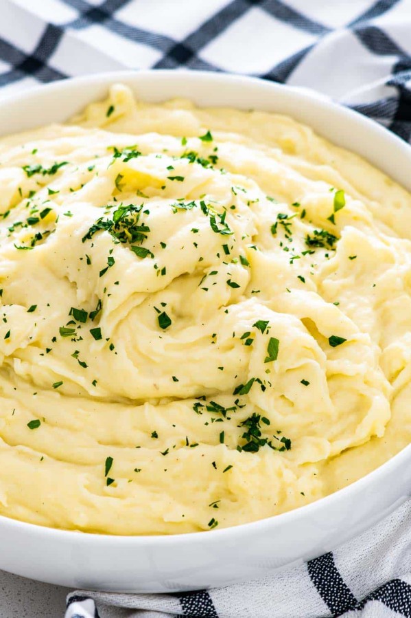 creamy mashed potatoes in a white bowl garnished with parsley.