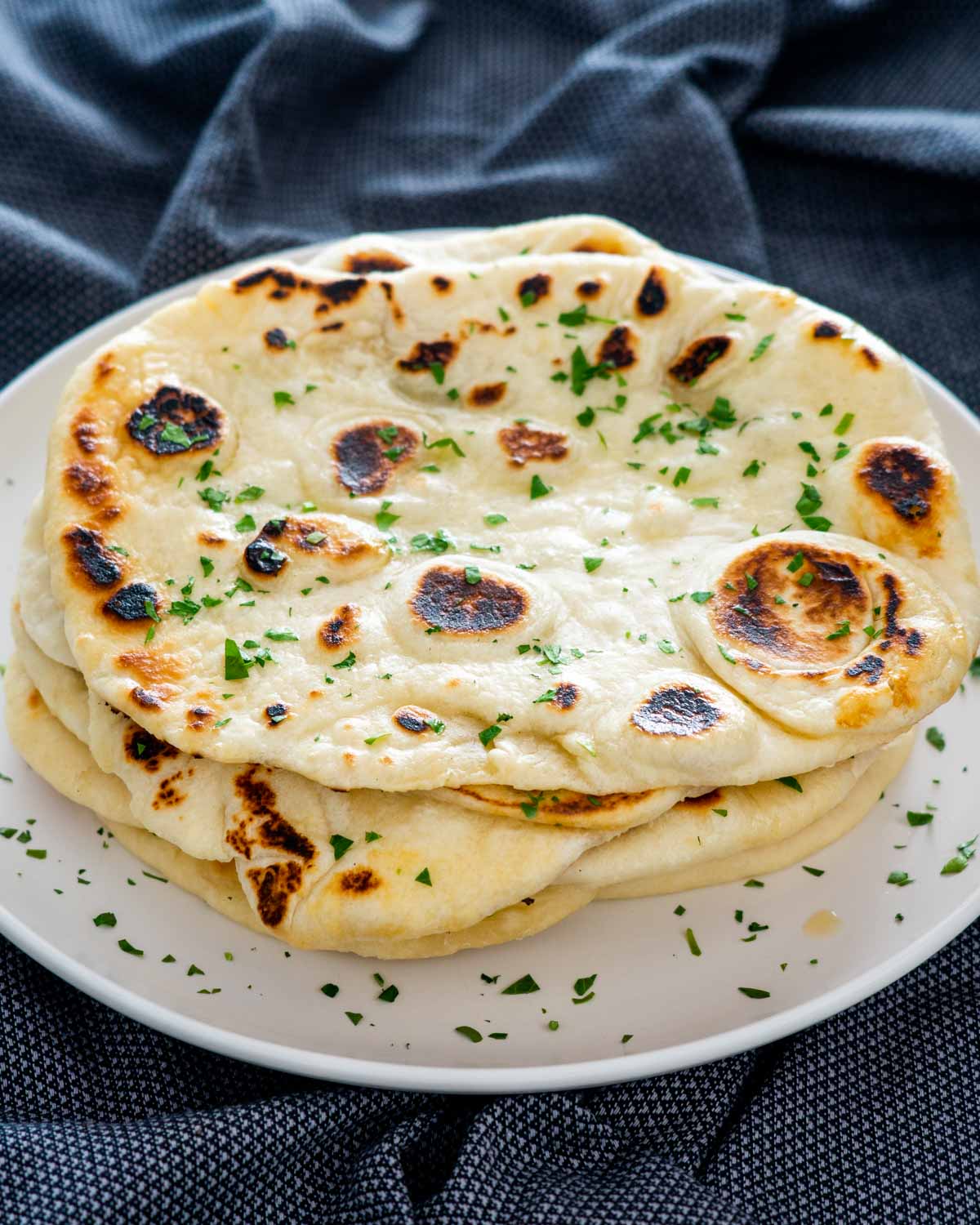stacked naan on a beige plate garnished with parsley.