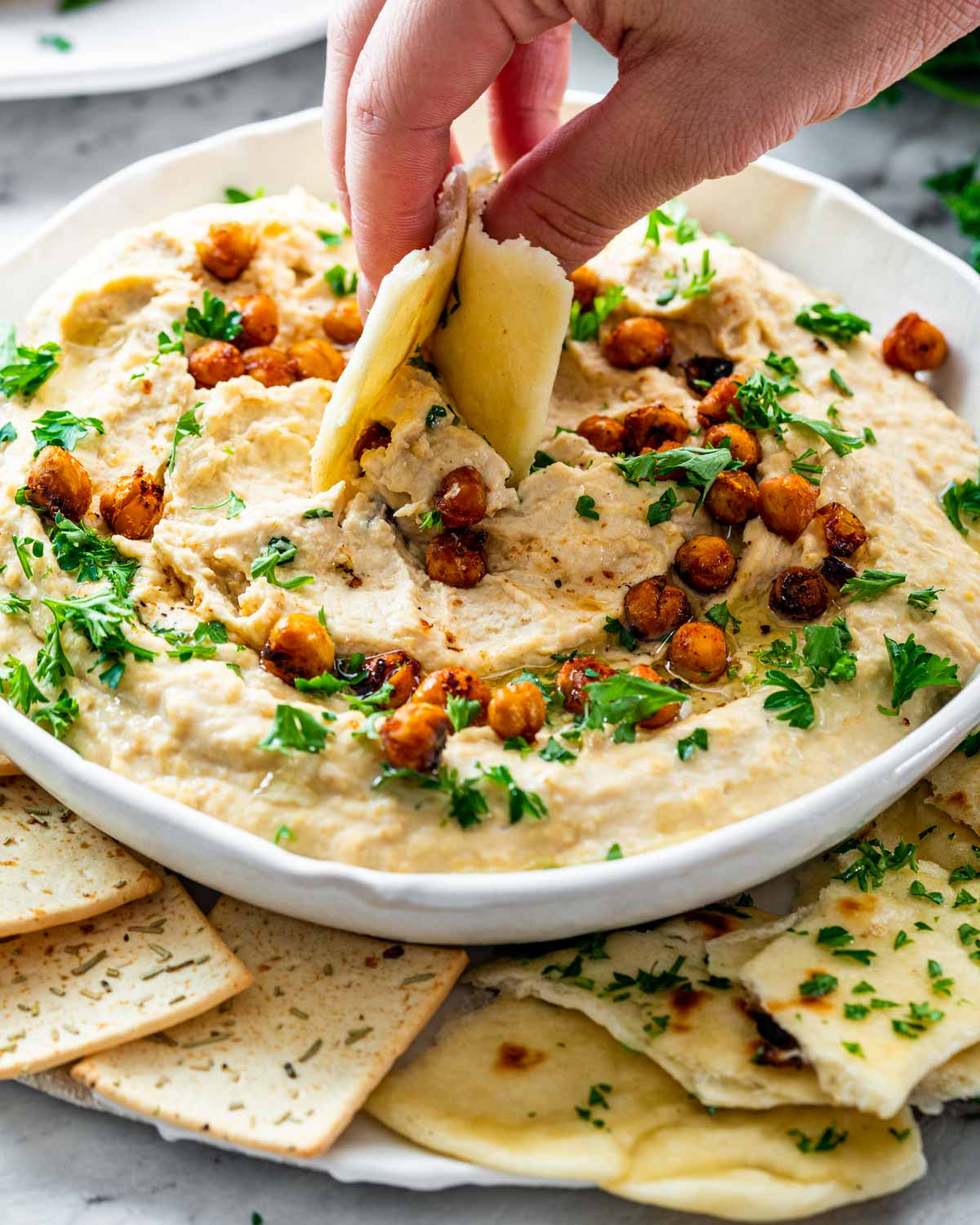 a hand dipping a piece of naan in homemade hummus.