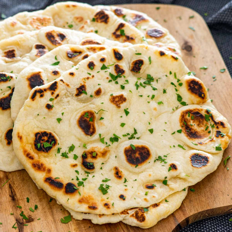 a bunch of naan on a cutting board garnished with parsley.