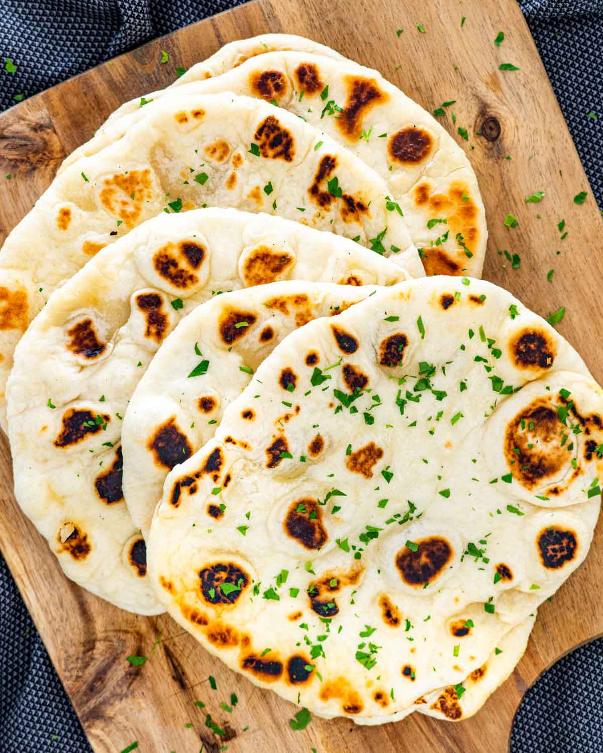 a bunch of naan on a cutting board garnished with parsley.