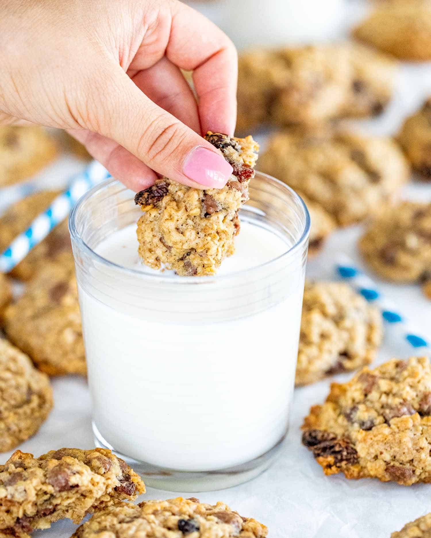 a hand dunking an oatmeal cookie in a glass of milk.
