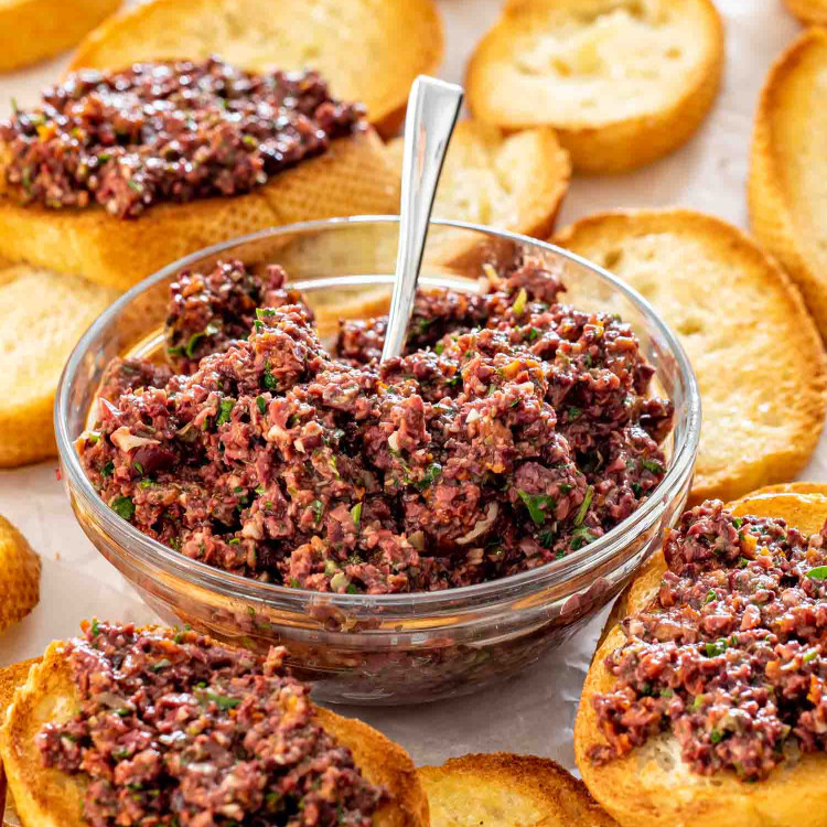 a bowl with olive tapenade surrounded by crostini.