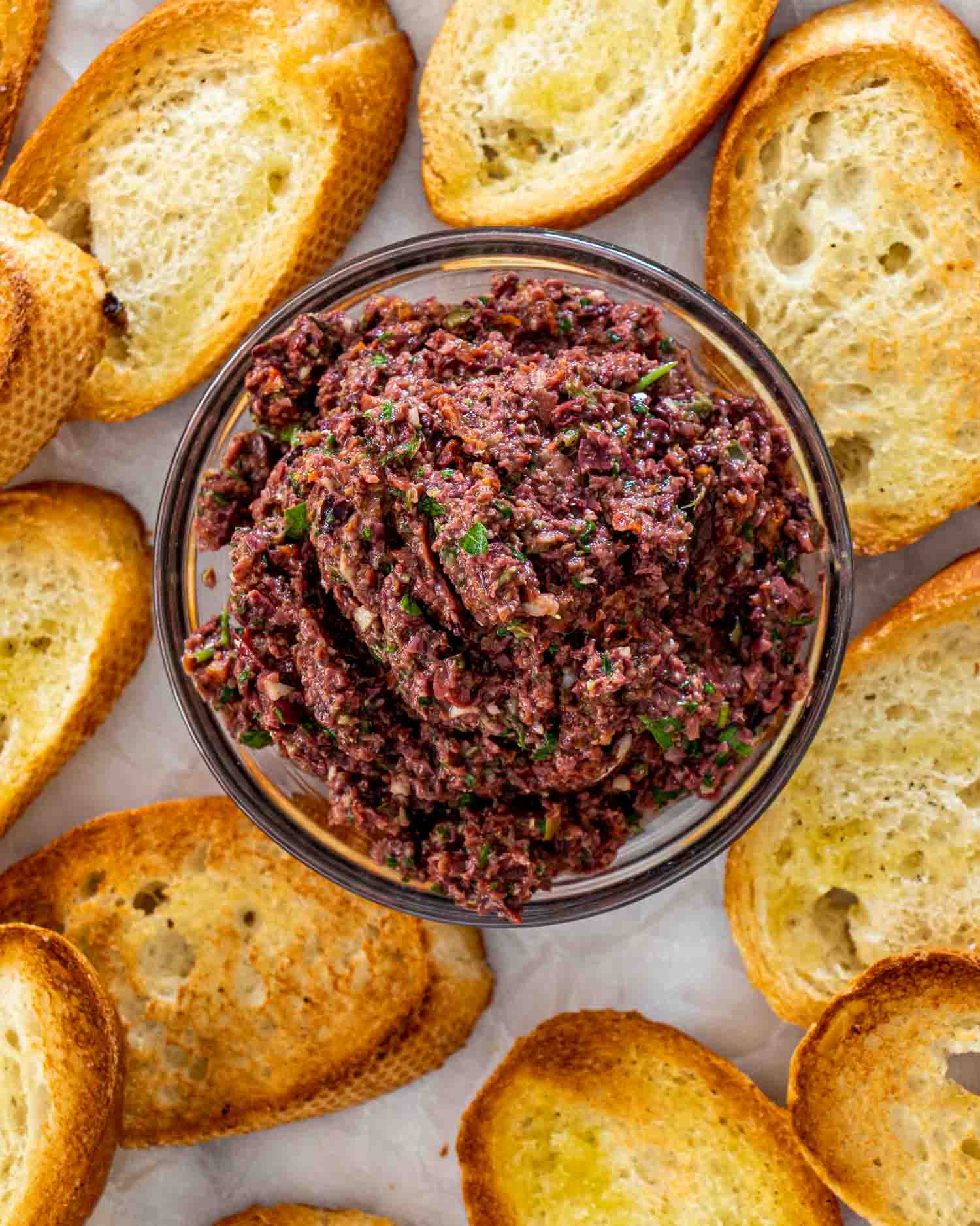 a bowl with olive tapenade surrounded by crostini.
