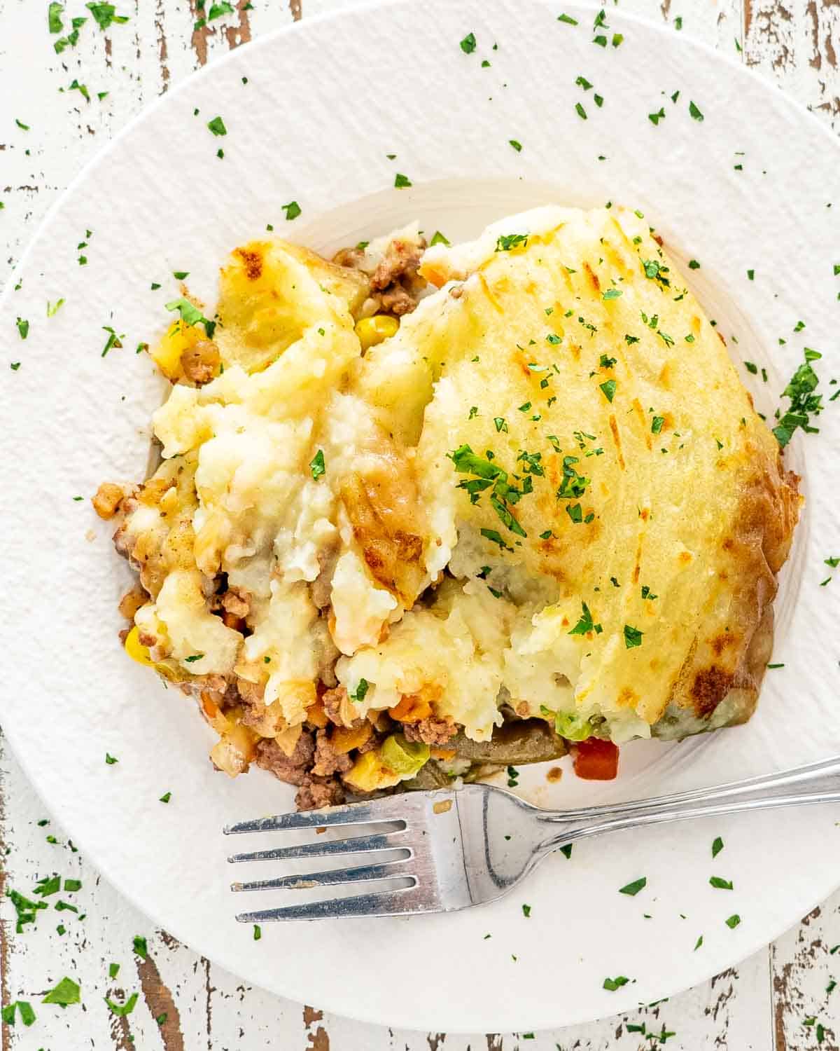 a serving of shepherd's pie in a white plate with a fork.