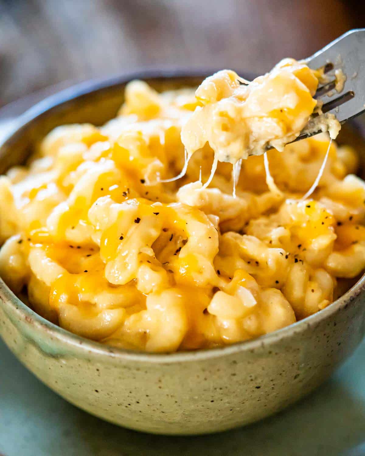 a bowl full of mac and cheese with a fork lifting some up.
