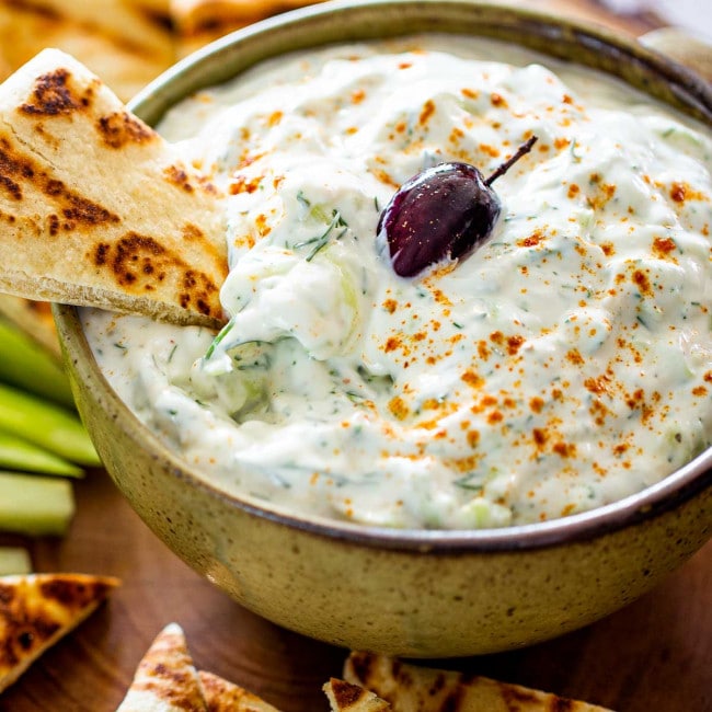 tzatziki sauce in a bowl with an olive on top surrounded by pita chips.