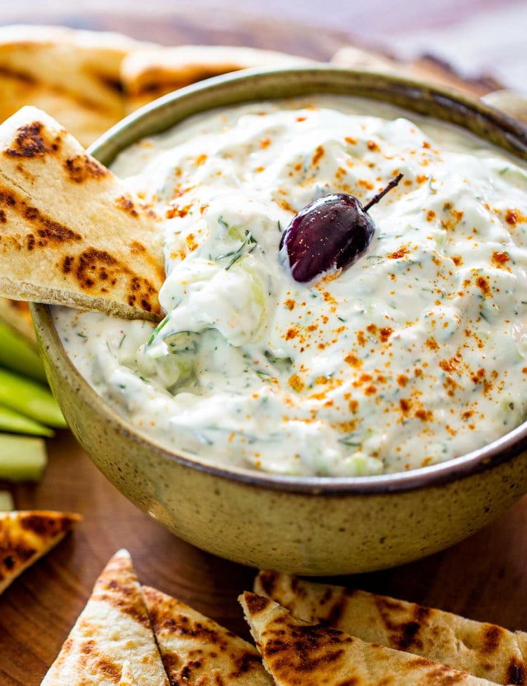 tzatziki sauce in a bowl with an olive on top surrounded by pita chips.