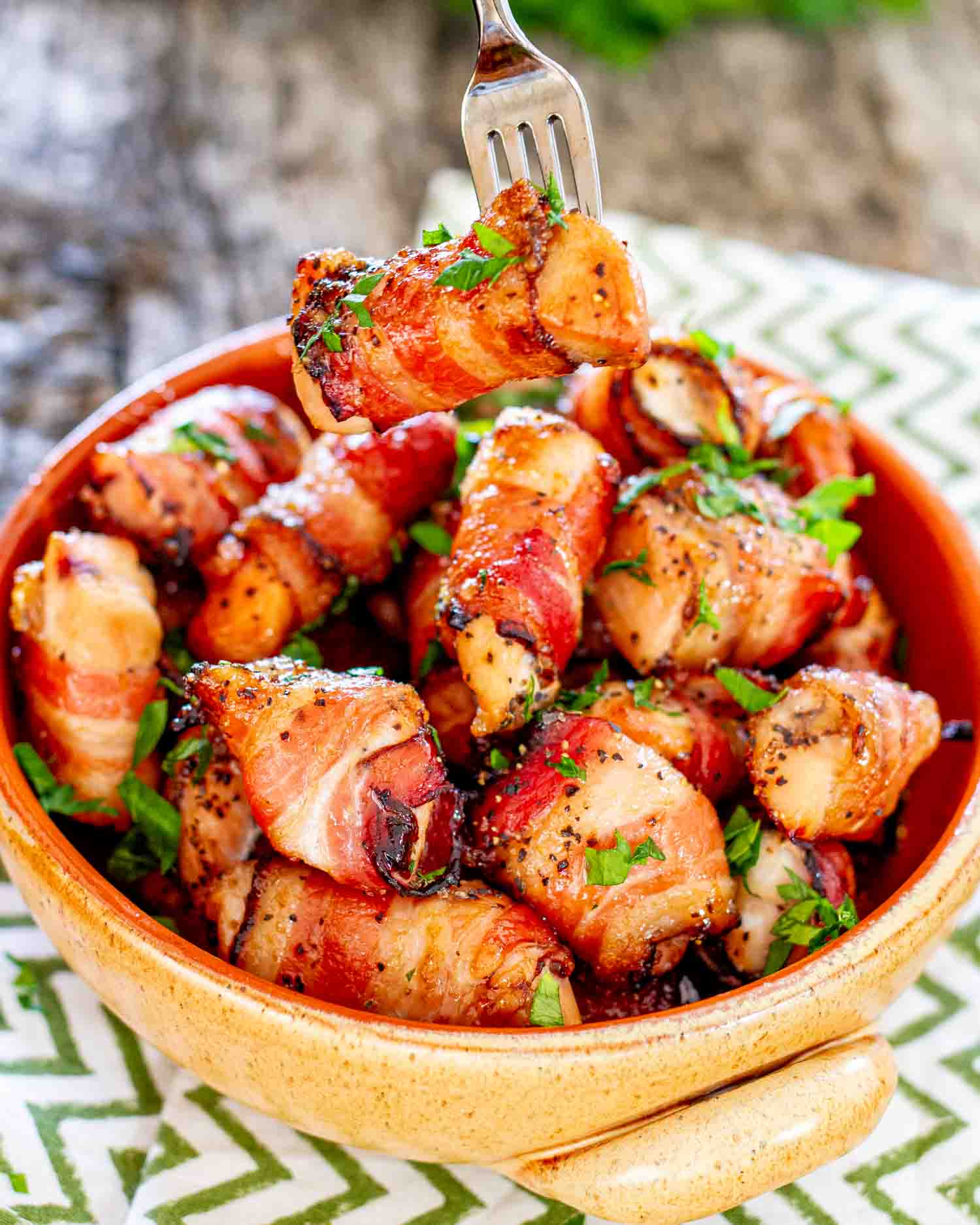 a few bacon wrapped chicken bites in a clay bowl garnished with parsley.