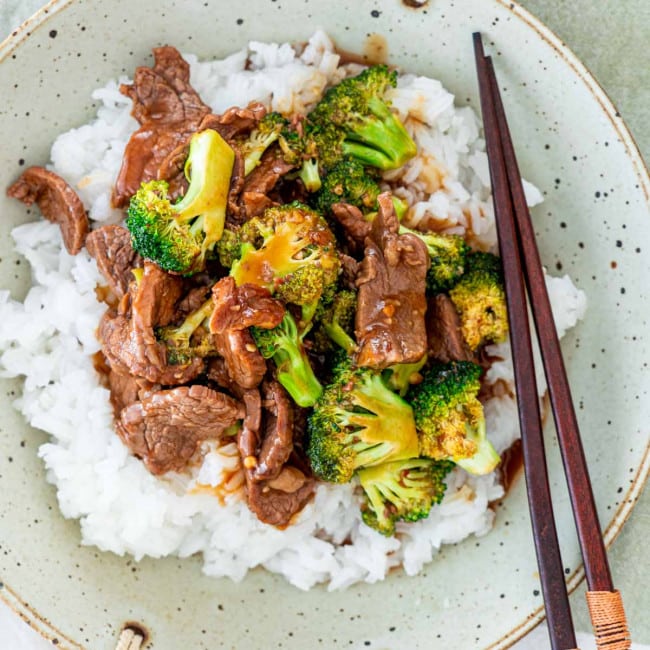 overhead shot of beef and broccoli on a bed of white rice, with chopsticks resting in the bowl