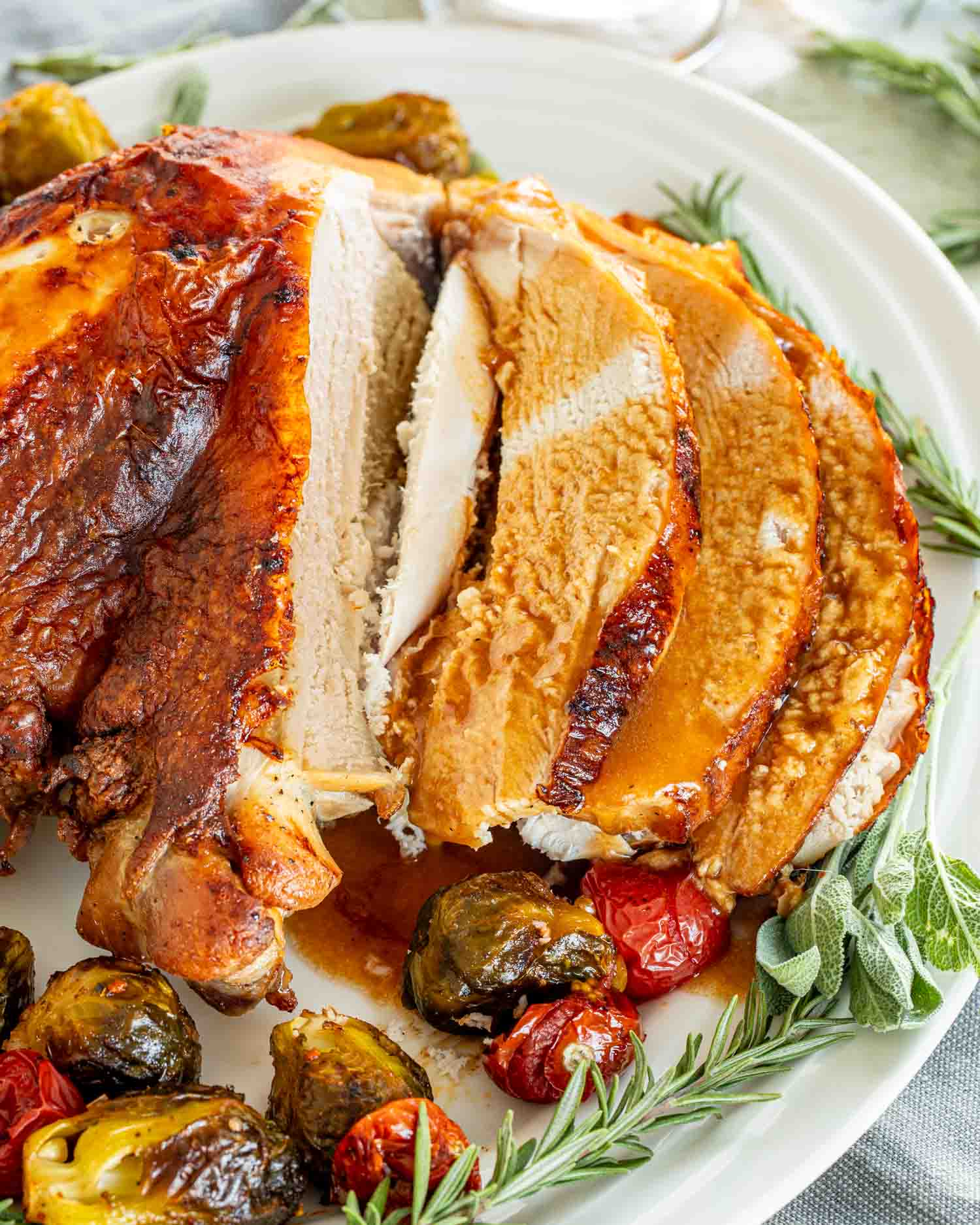 a brined roast turkey breast sliced up with lots of turkey gravy on a white turkey platter.