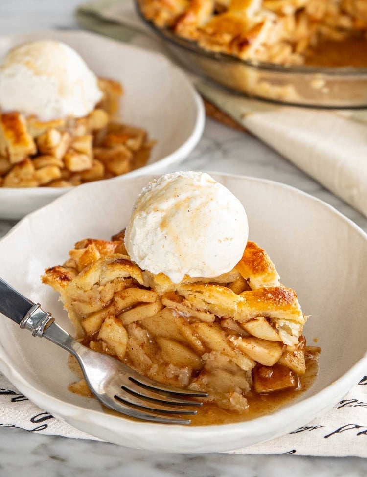 a slice of apple pie in a white bowl with a scoop of ice cream.
