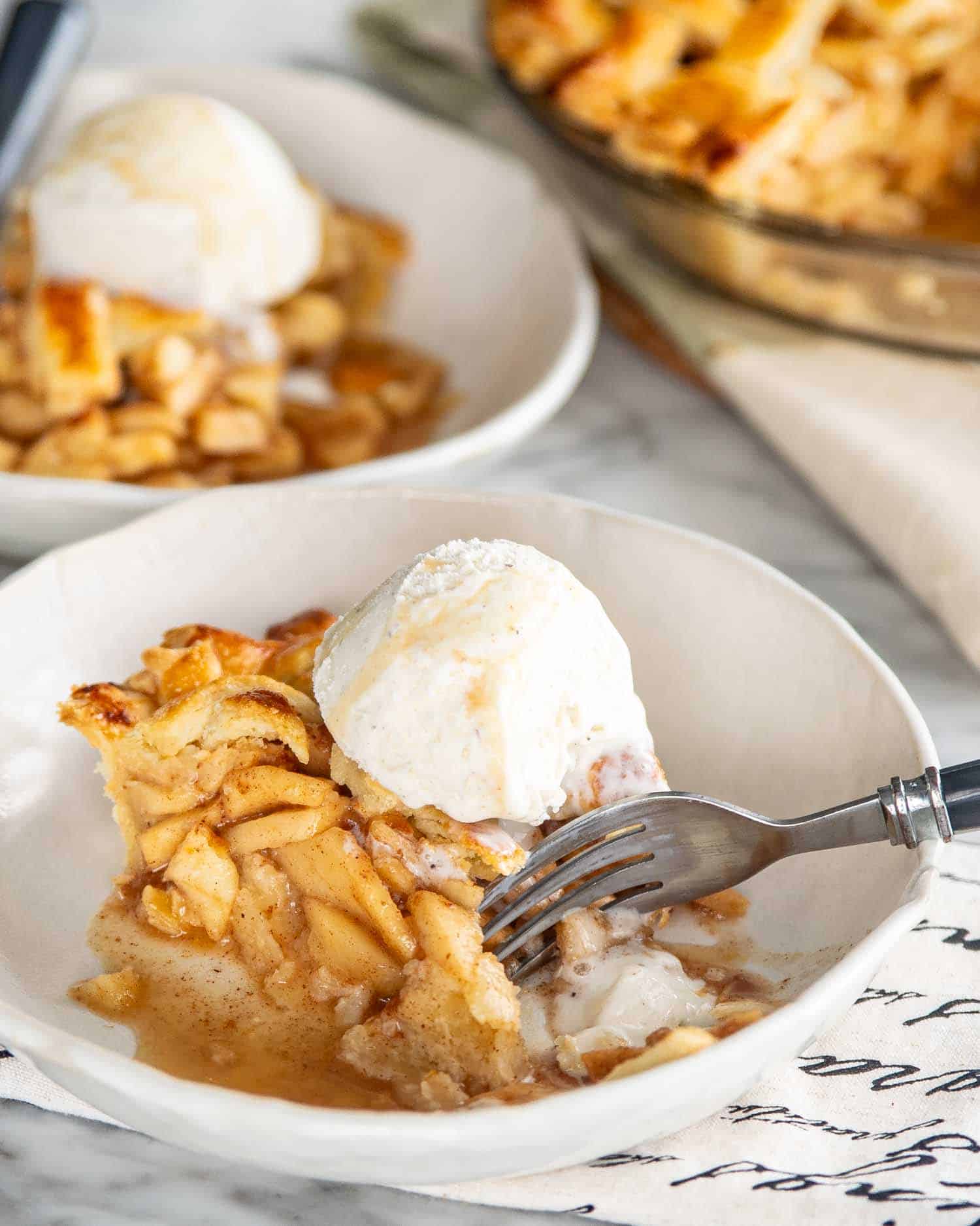 a slice of apple pie in a white bowl with a scoop of ice cream.
