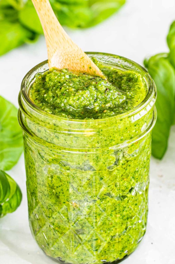 homemade pesto in a jar with some basil around it.