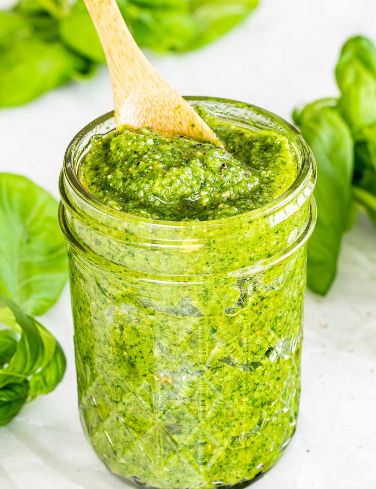 homemade pesto in a jar with some basil around it.