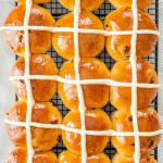 freshly baked hot cross buns on a black cooling rack.