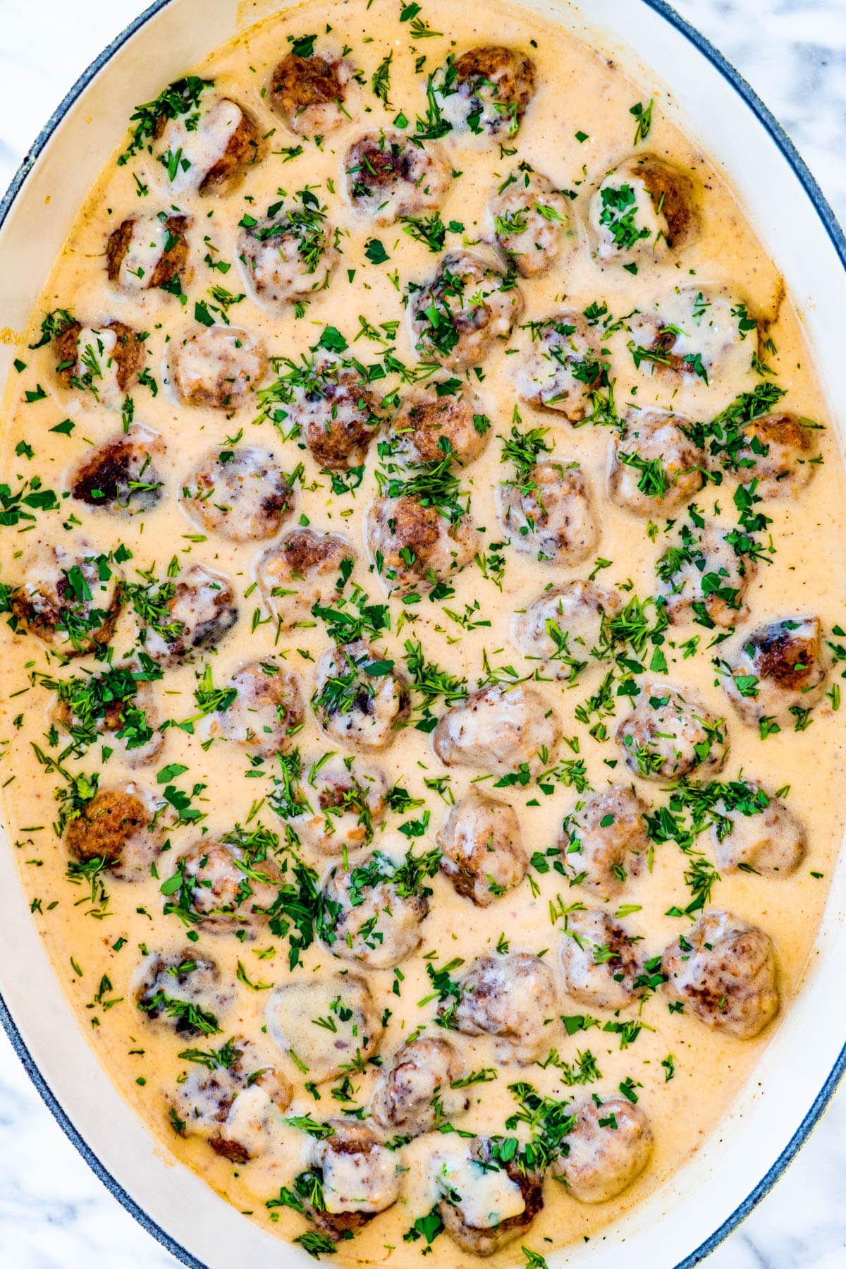 overhead shot of swedish meatballs in an oval casserole dish garnished with dill and parsley