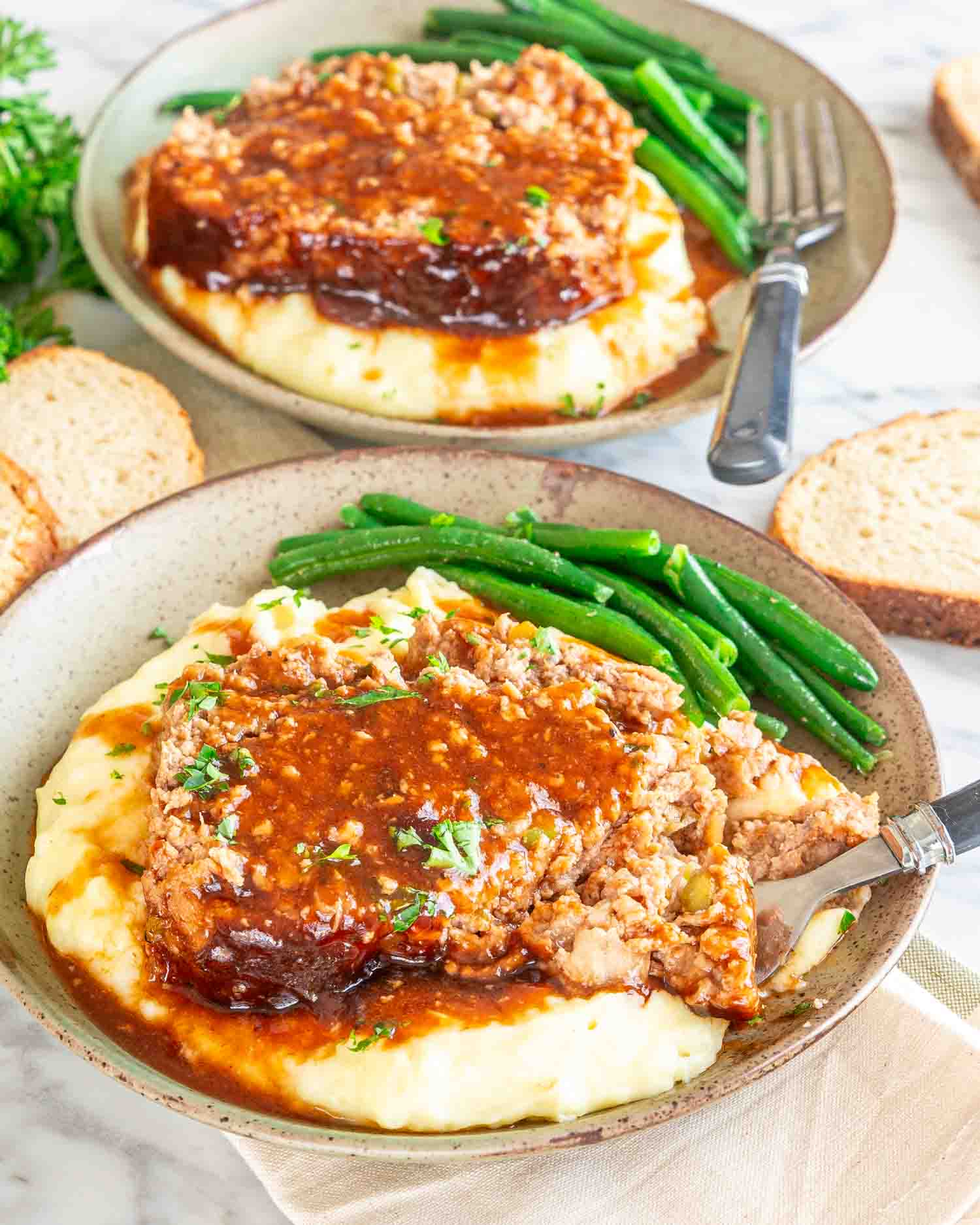 a slice of meatloaf on a bed of mashed potatoes along some green beans.