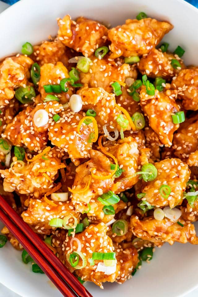 closeup of orange chicken in a white bowl garnished with sesame seeds and green onions