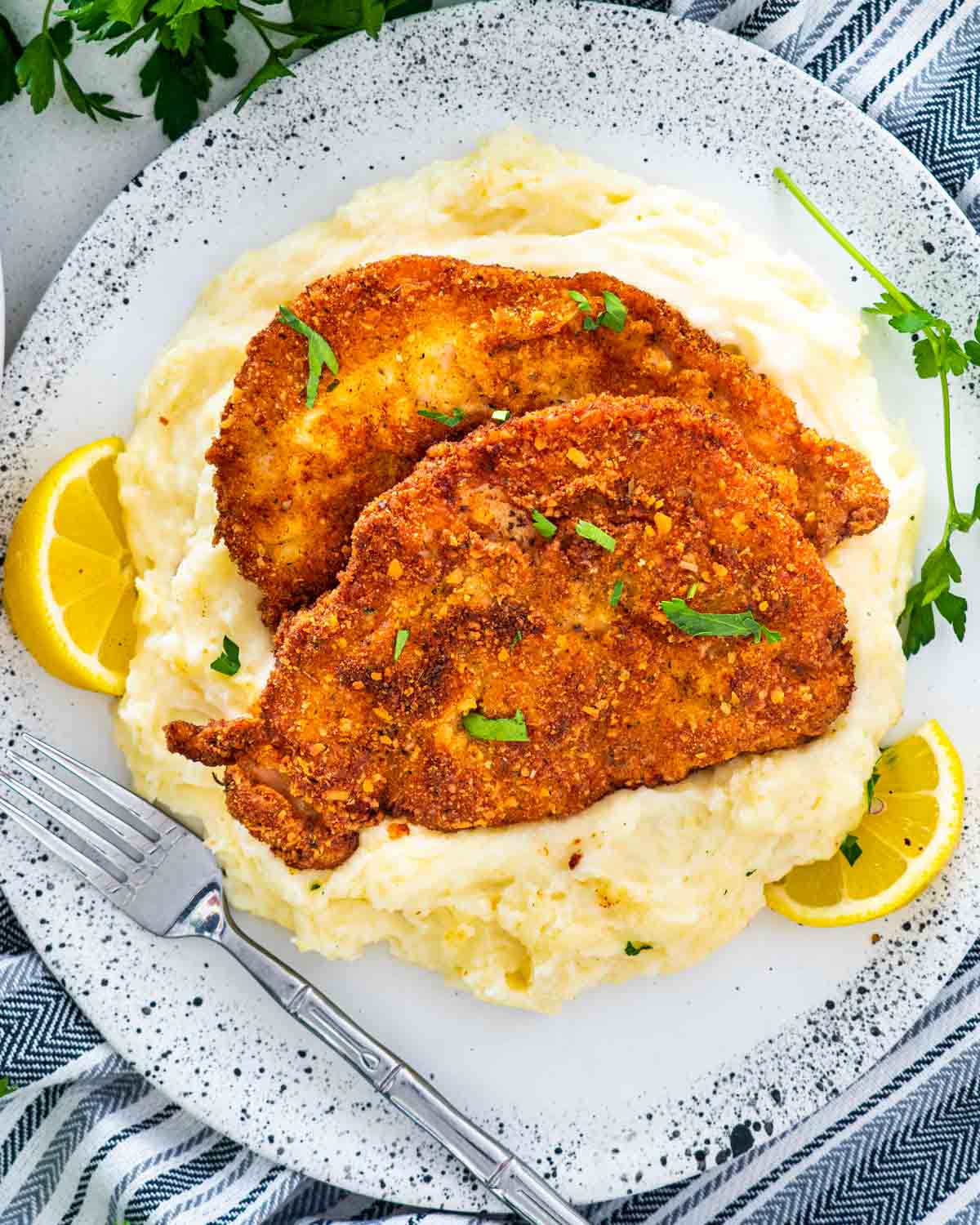 2 pork schnitzel over a bed of mashed potatoes on a plate.