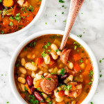 overhead shot of a bowl of sausage and bean soup with a spoon in it