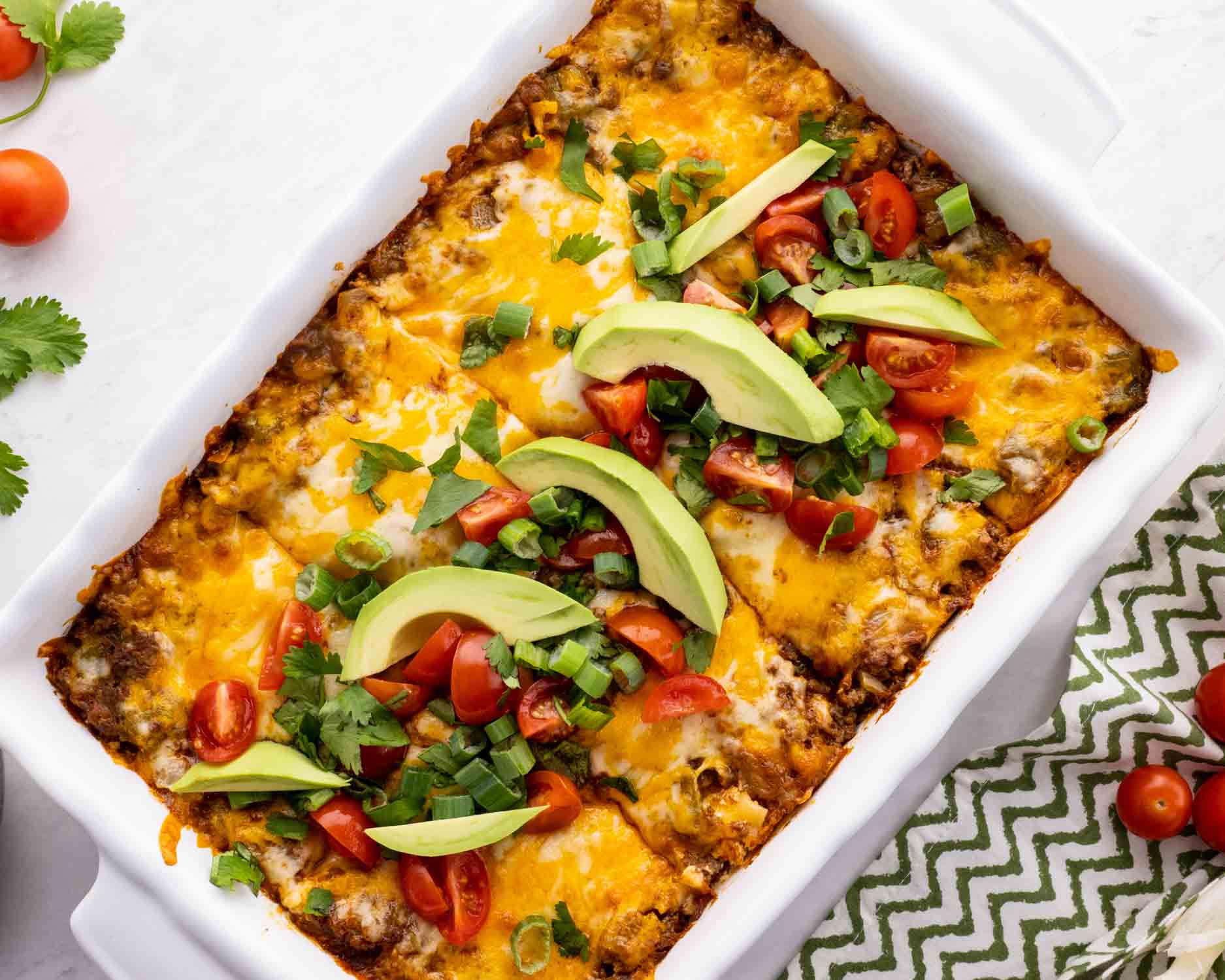 freshly made taco lasagna in a white casserole dish garnished with tomatoes and avocado.