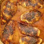 Top-down view of six baked chicken breasts in a deep dish, coated in rich, seasoned pan juices.