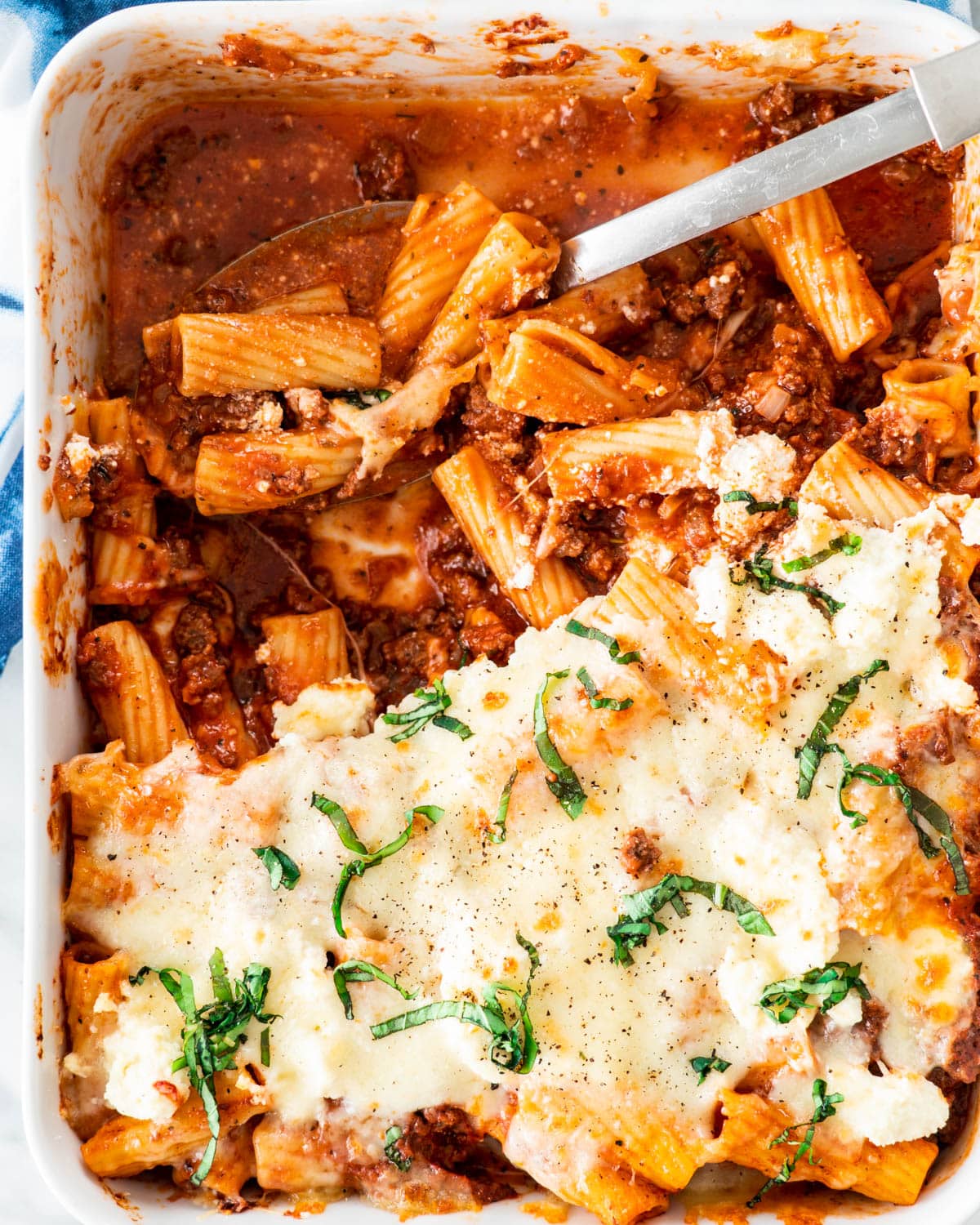 overhead shot of baked ziti in a casserole dish with a serving spoon 