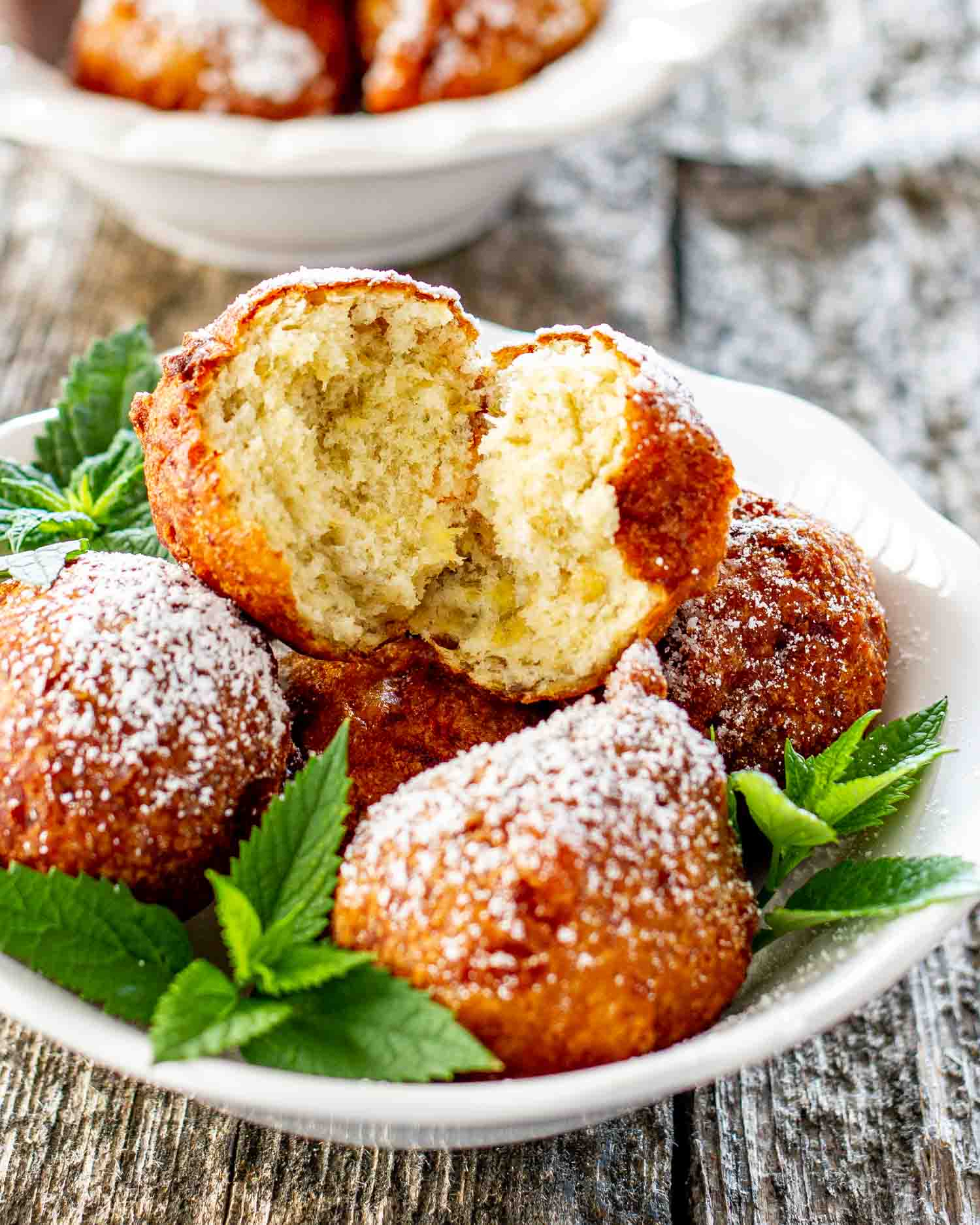 a few banana fritters with mint and sprinkled with powdered sugar in a white bowl.