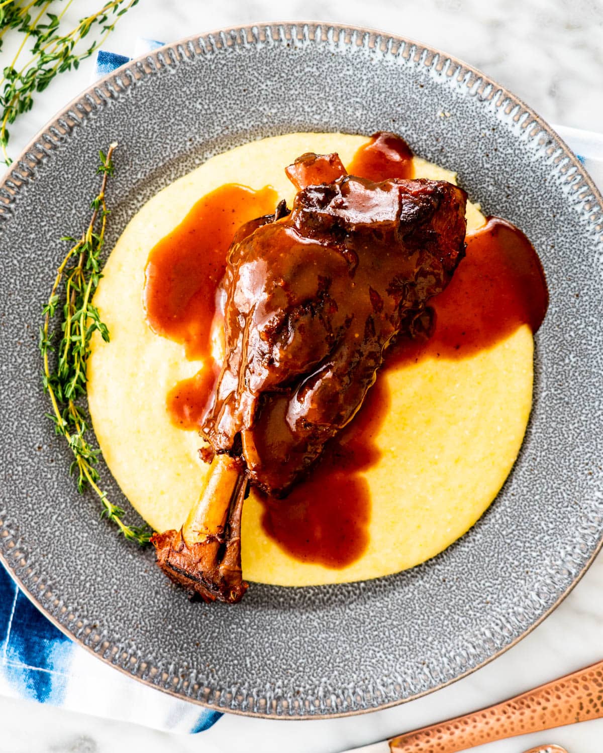 overhead shot of a braised lamb shank over creamy polenta with sauce on it