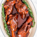 overhead shot of braised lamb shanks in a pot with two sprigs on rosemary