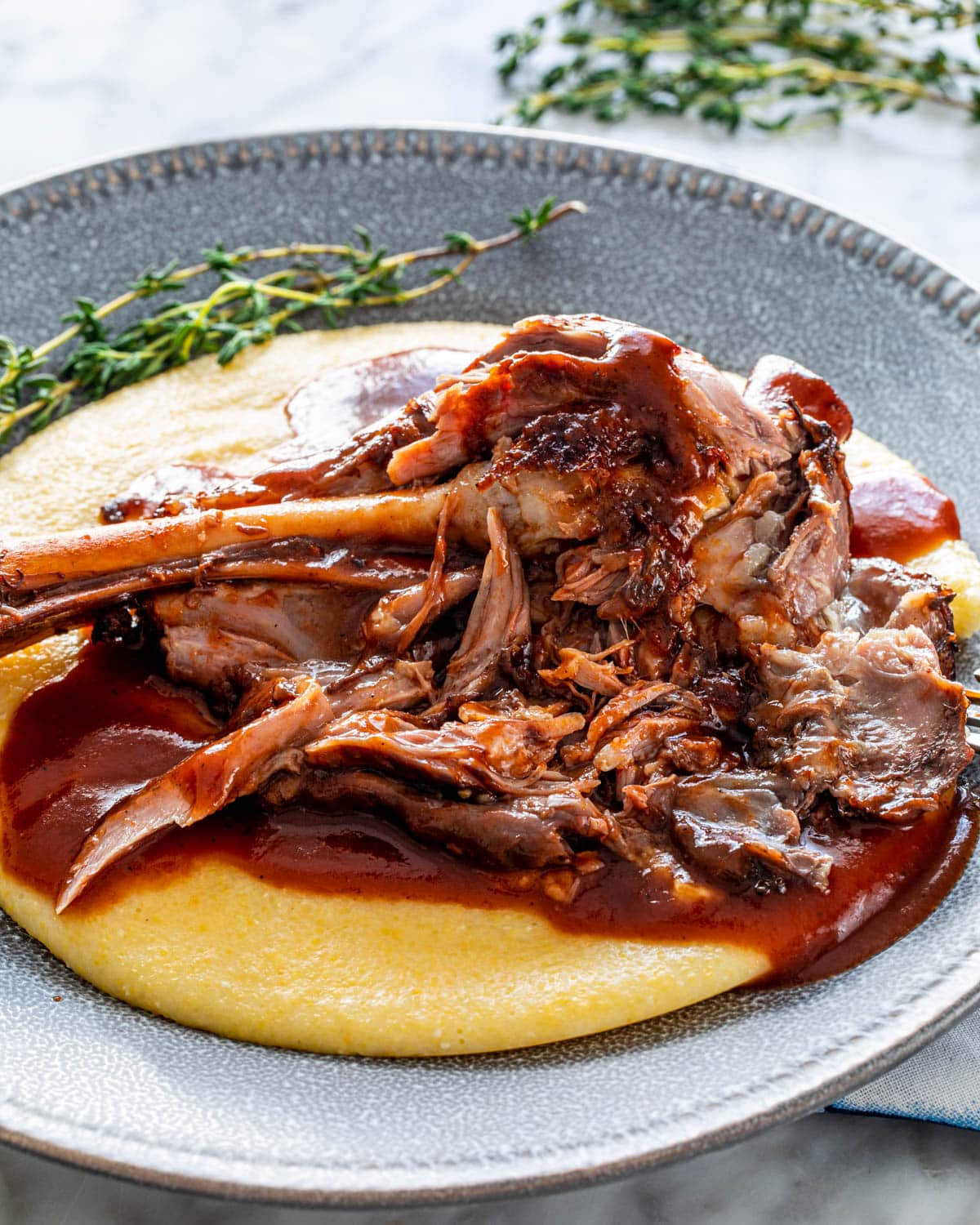 a lamb shank with sauce over creamy polenta in a grey plate