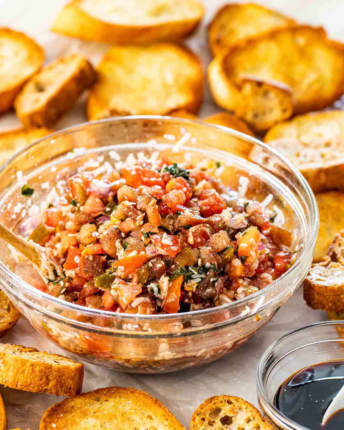 bruschetta in a bowl with toasted baguette slices around it.