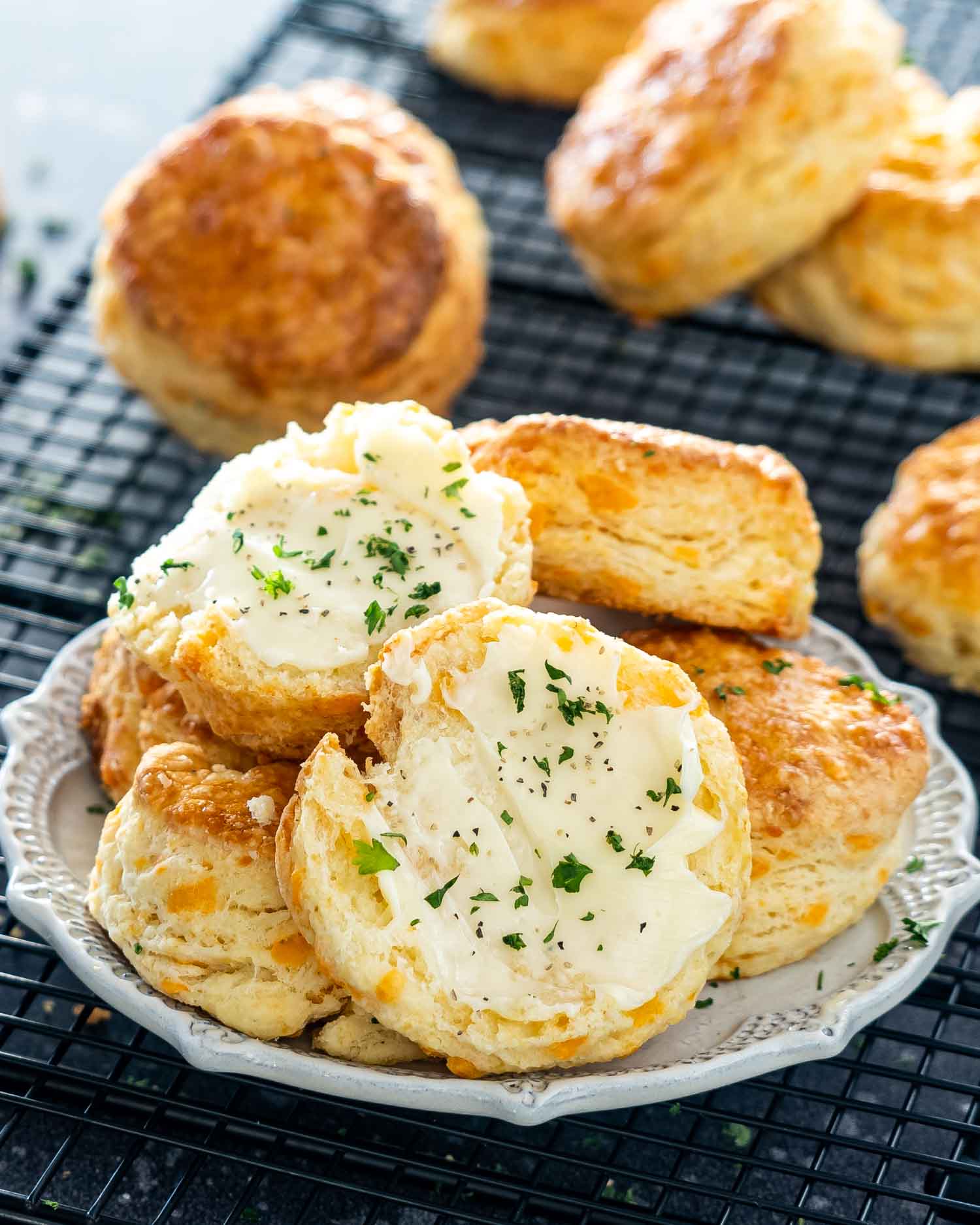 a few cheese biscuits on a beige plate with the top one broken in half and with butter.