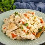 Creamy chicken rice pilaf served on a green plate with carrots, peas, and parsley, ready to eat.