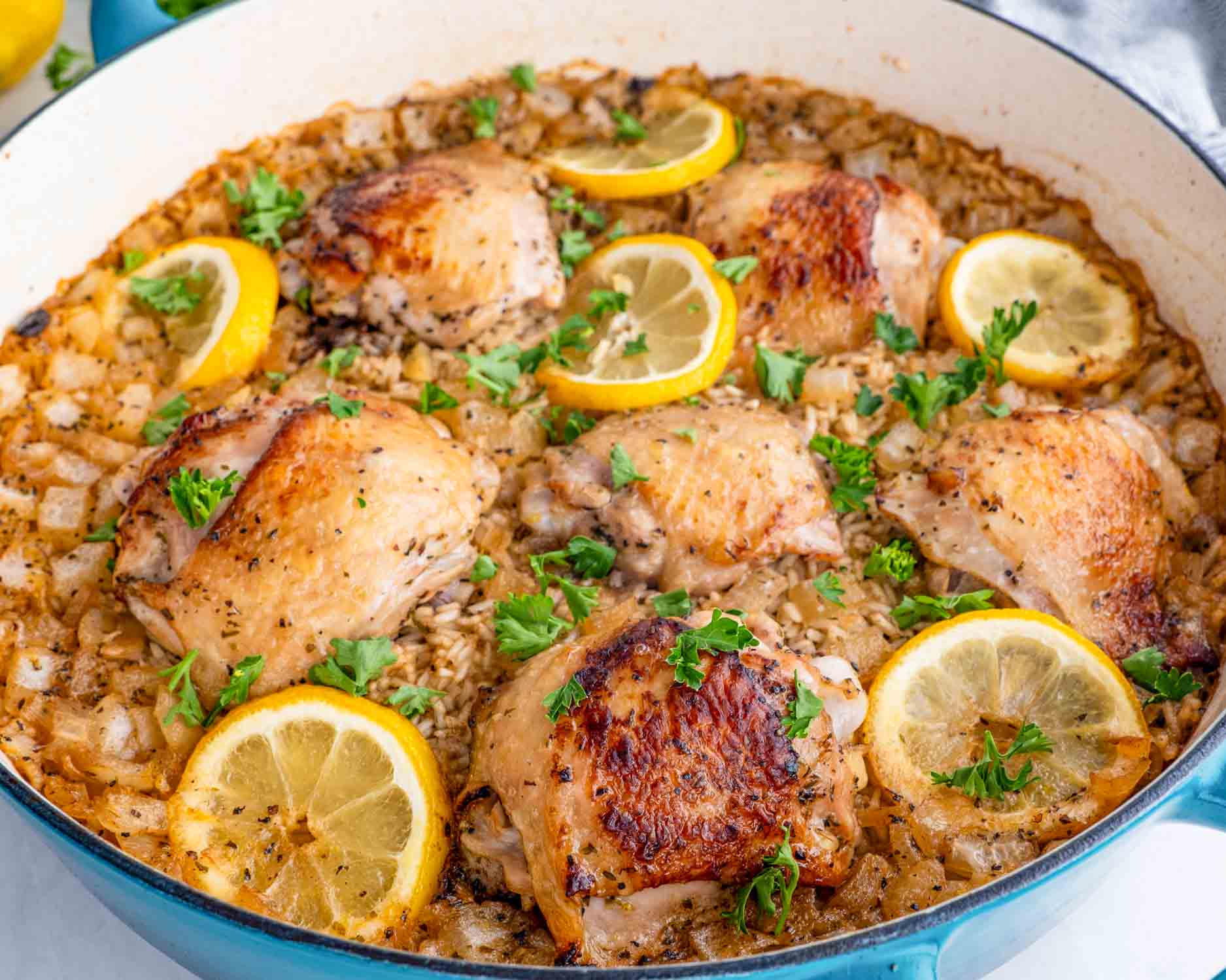 lemon chicken rice bake in a blue dutch oven garnished with parsley.
