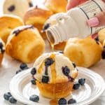 a hand pouring maple syrup on a pancake muffin.
