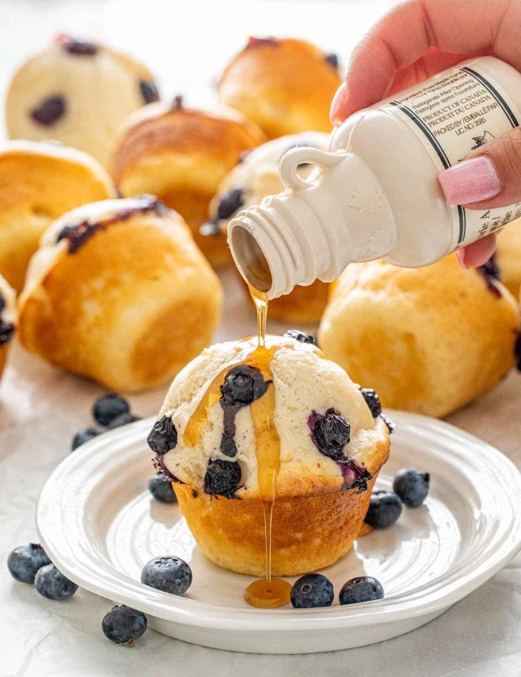 a hand pouring maple syrup on a pancake muffin.