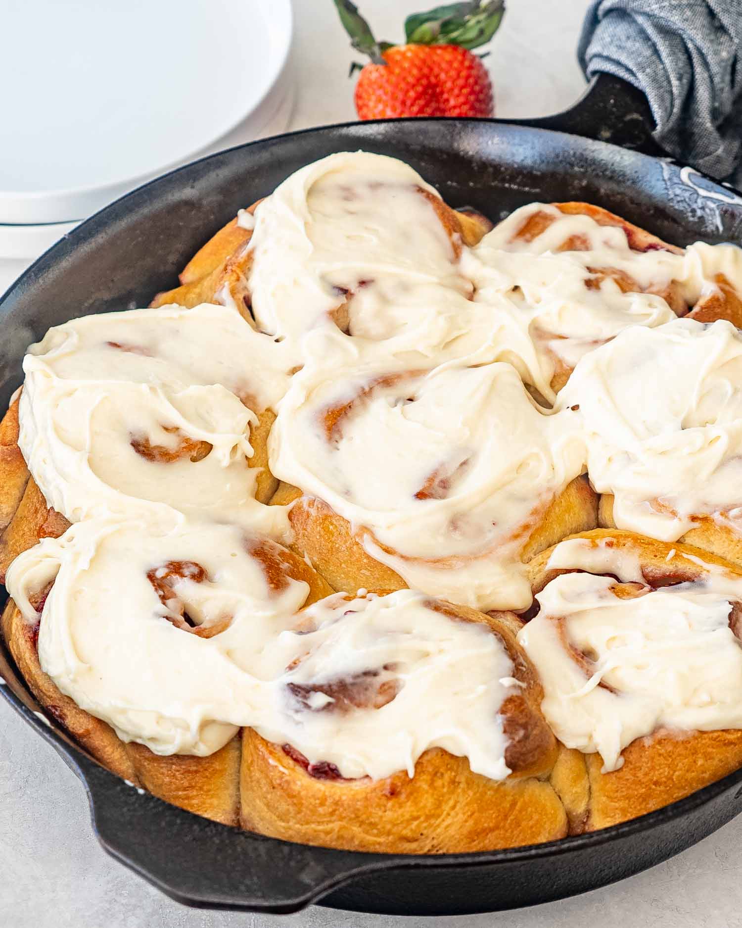 strawberry rolls with cream cheese icing in a cast iron skillet.