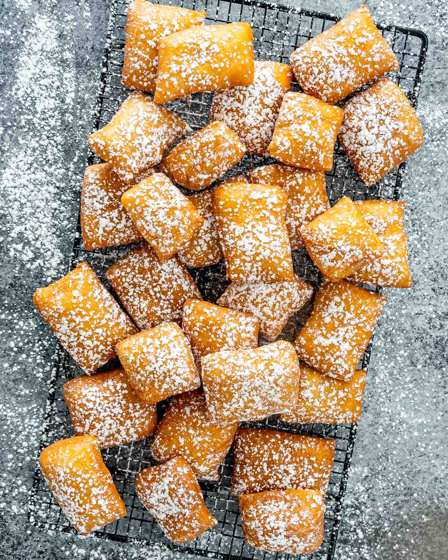freshly made beignets on a cooling rack with powdered sugar.