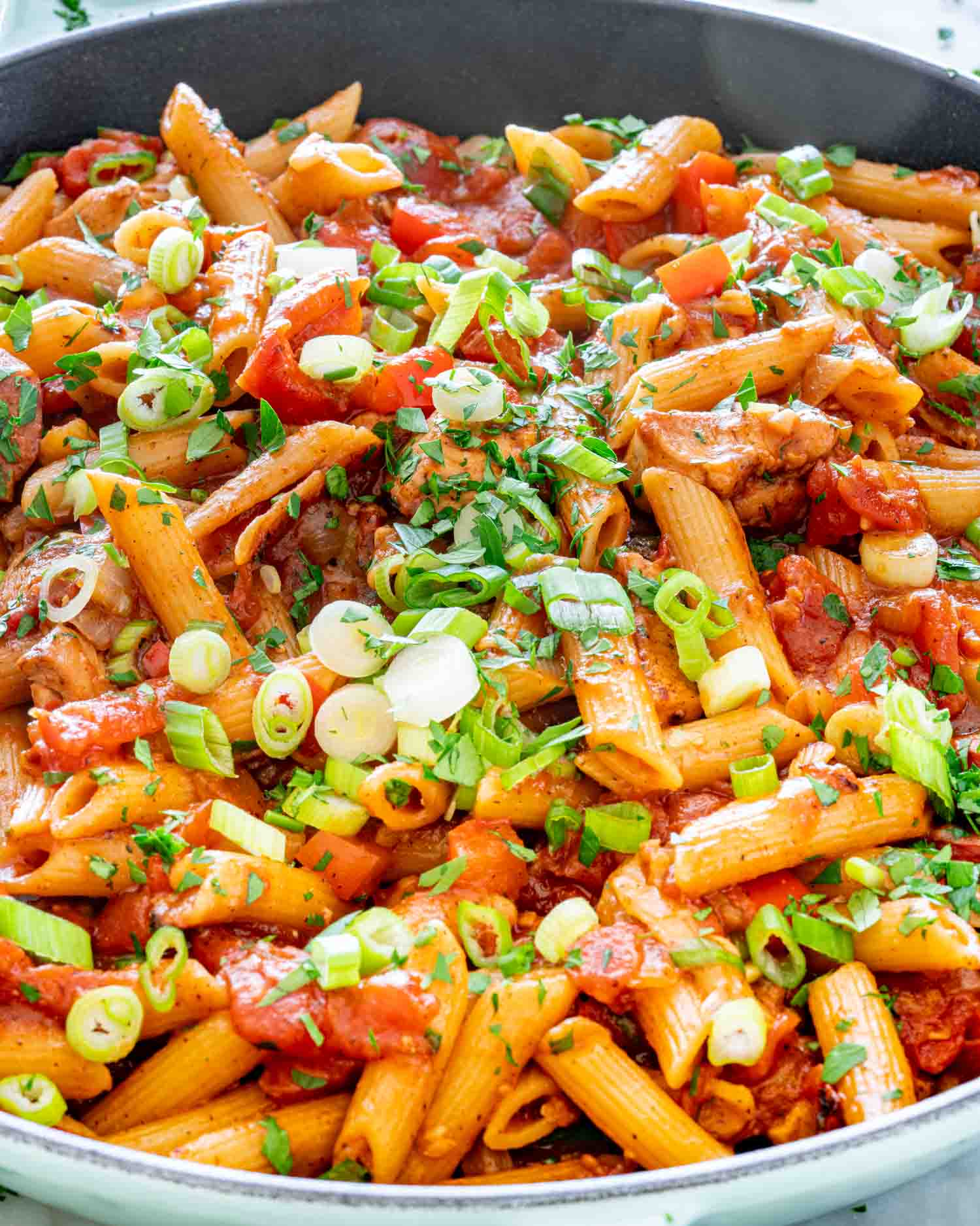 chicken and sausage penne jambalaya in a skillet garnished with green onions.