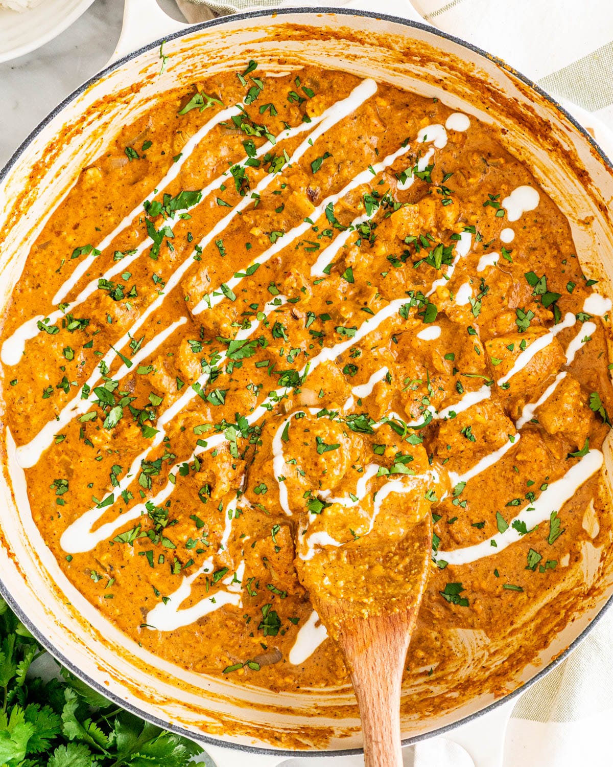 overhead shot Chicken Korma in a skillet garnished with yogurt and cilantro