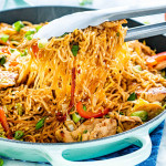 side view shot of tongs lifting chicken ramen stir fry out of a skillet