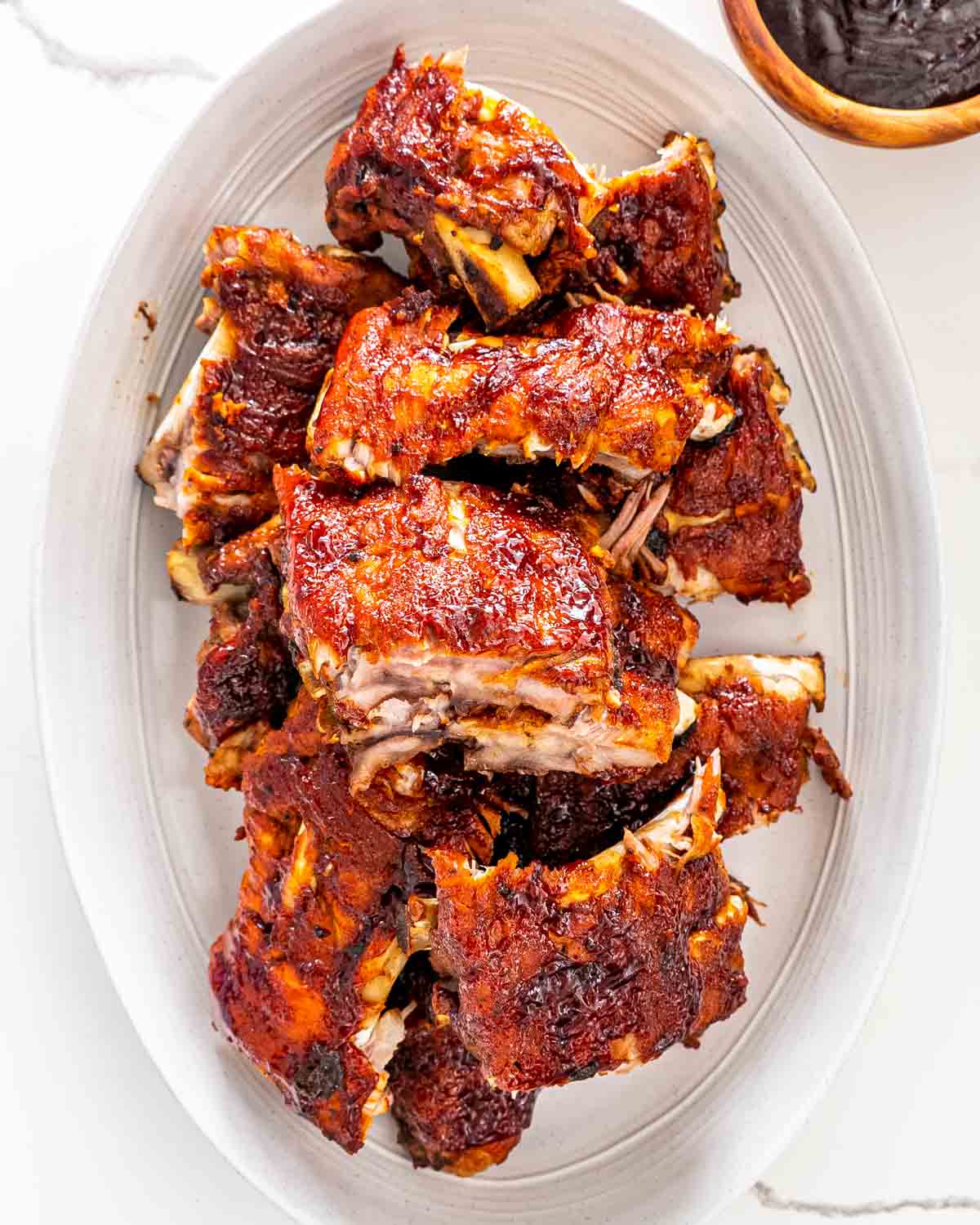cut up bbq ribs on a white serving platter.