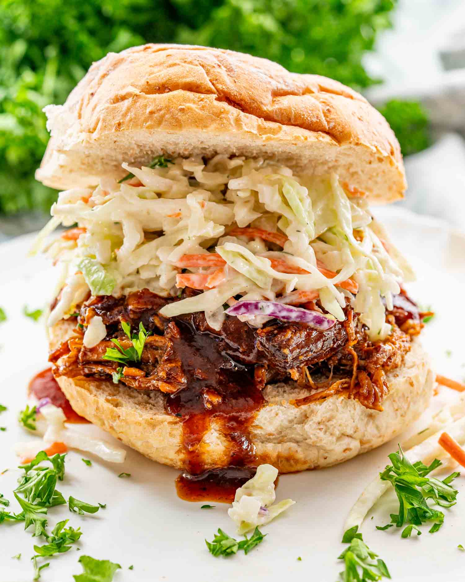 a pulled pork sandwich on a bun with lots of coleslaw and bbq sauce.
