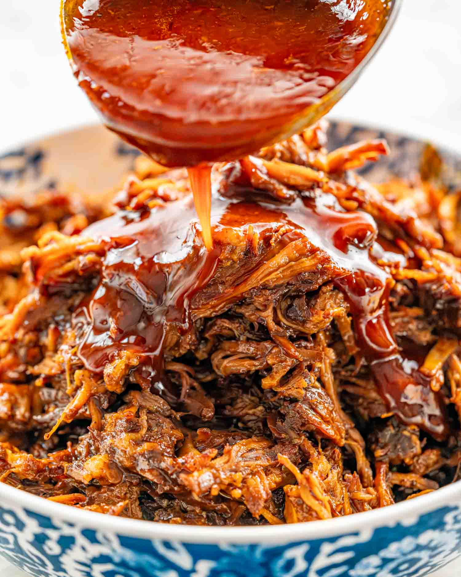a ladle pouring bbq sauce over pulled pork.